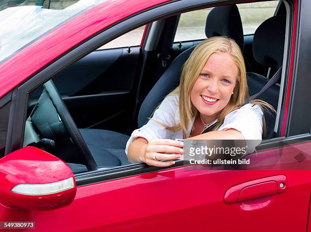 Eine junge Frau zeigt stolz ihren Führerschein. Fahrerlaubnis und neues Auto.