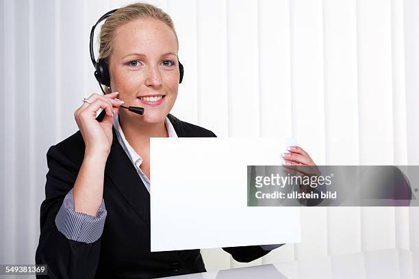 Eine freundliche junge Frau mit Headset im Kundendienst telefoniert mit einem Kunden. Freundliche Hotline Mitarbeiterin.