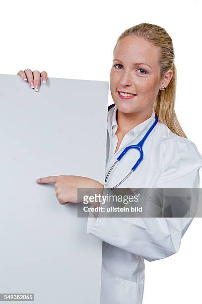 Eine junge Ärztin mit Stethoskop in ihrer Arztpraxis. Hält ein leeres Schild in der Hand