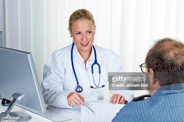 Eine junge Ärztin mit Stethoskop in ihrer Arztpraxis. Im Gespräch mit einem Patienten
