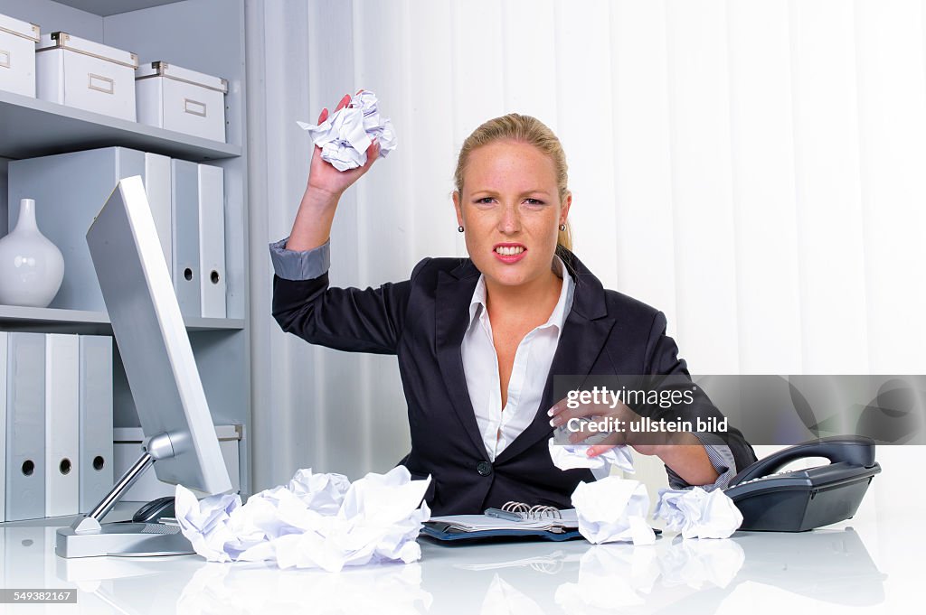 Eine Frau im Büro wirft mit zusammengeknülltem Papier.  Ärger, Stress und Frust am Arbeitsplatz