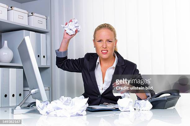 Eine Frau im Büro wirft mit zusammengeknülltem Papier. Ärger, Stress und Frust am Arbeitsplatz