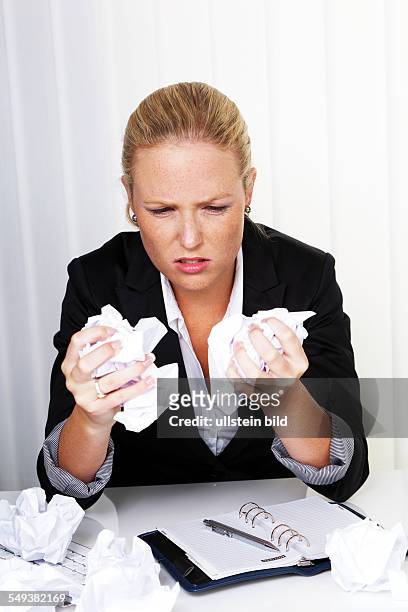 Eine Frau im Büro mit zusammengeknülltem Papier. Ärger, Stress und Frust am Arbeitsplatz