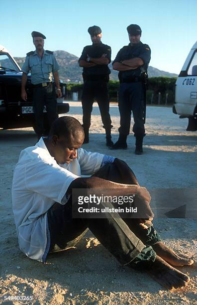 Spain, Tarifa: Arrest and transport of immigrants at the beach of Tarifa by the Guardia Civil. A migrant sits on the floor and is guarded by three...