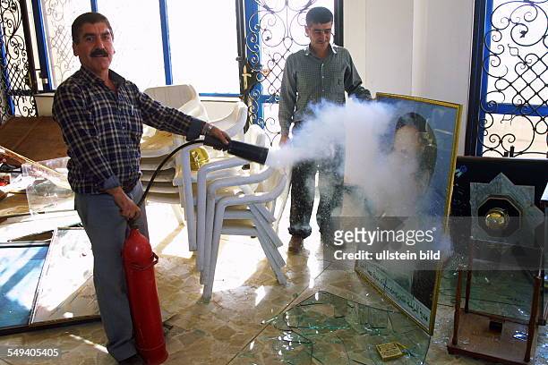 Iraq, Baghdad: Destruction and plunder in the Saddam History Museum after the fights. Men extinguish the fire at a picture, in their back: stacked...