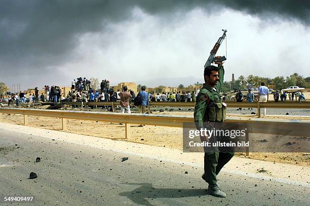 Iraq, Baghdad: A soldier holds a machine gun in the air. Clouds of smoke in heaven. In the background are some bystanders