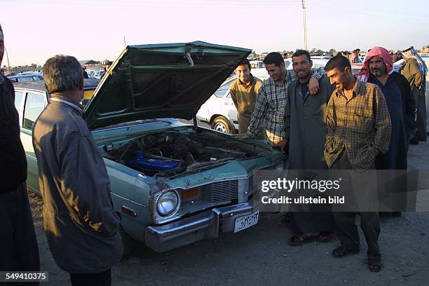 Iraq, Baghdad: The private second hand car market: Men stand next to a car with open bonnet