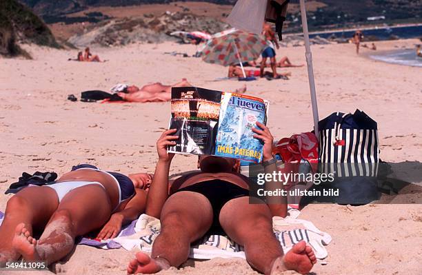 Spain, Tourists sun themselves and read magazines over immigration.