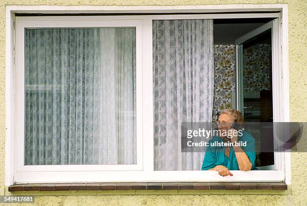 Germany, 1998: Communication; a senior citizen with a mobile phone at the window.