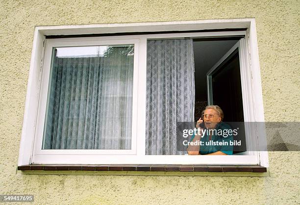 Germany, 1998: Communication; a senior citizen with a mobile phone at the window.