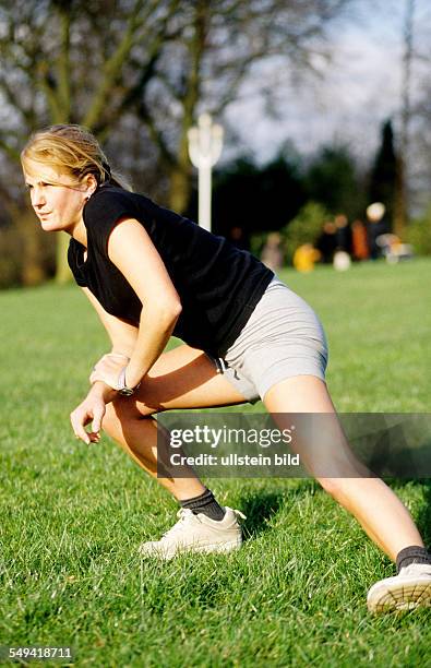 Germany, Essen: A young woman stretching; in the Gruga Park.