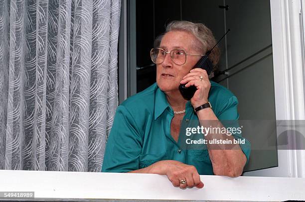 Germany, 2001: Communication, media, senior citizen calls with a cellular phone at the window.