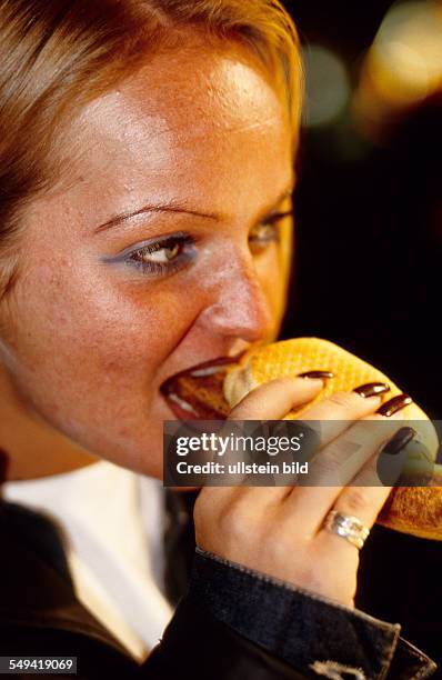 Germany, Dortmund: Food and drinks.- A young woman eating a bratwurst.