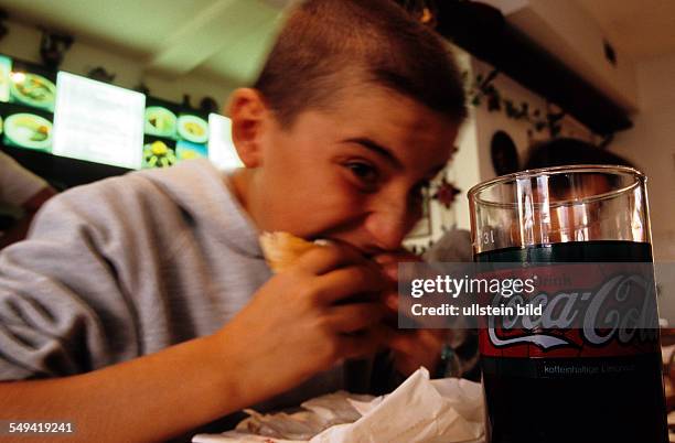 Germany, Usingen: A young boy eating a doener kebab in a Turkish snack-bar, a Coca Cola to drink.