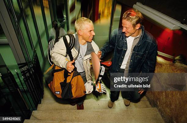 Germany: Free time.- Two young men going up a staircase; one of them is carriing a snowboard under his arm.