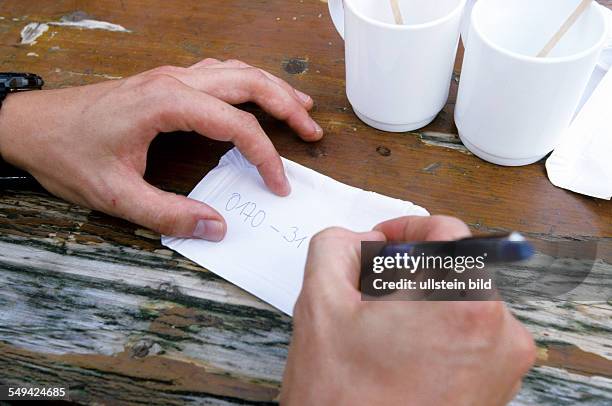 Germany: Free time.- Young persons in a cafe; the man is writing his phone number on a piece of paper.