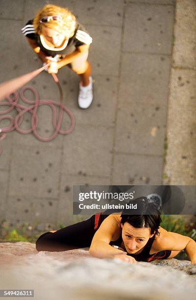 Germany: Free time.- A young woman climbing up a stone wall.