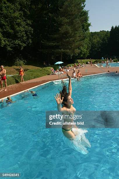 Germany, : In a swimming pool; a young woman jumping into the water.