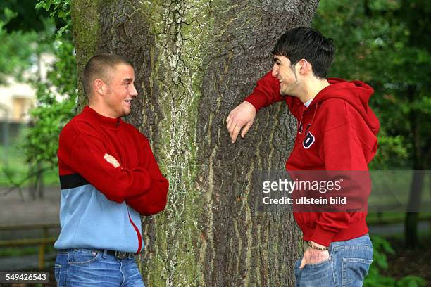 Germany, : Portrait of two young persons; they are leaning against a tree talking.