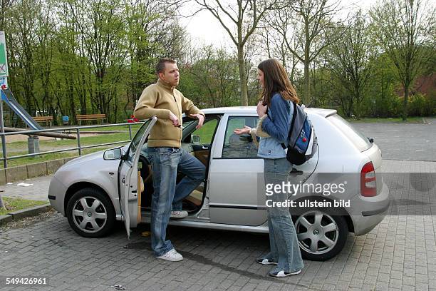 Germany, : Free time.- Young persons at a car park; a woman and a man stand next to a car discussing.