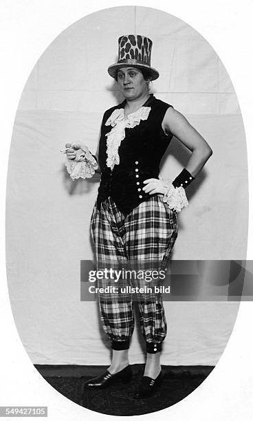 Germany, Berlin about 1922: Woman in a costume. Sie wears a top hat with a leopards swatch, a vest with frills, a checked trousers and gloves. In her...