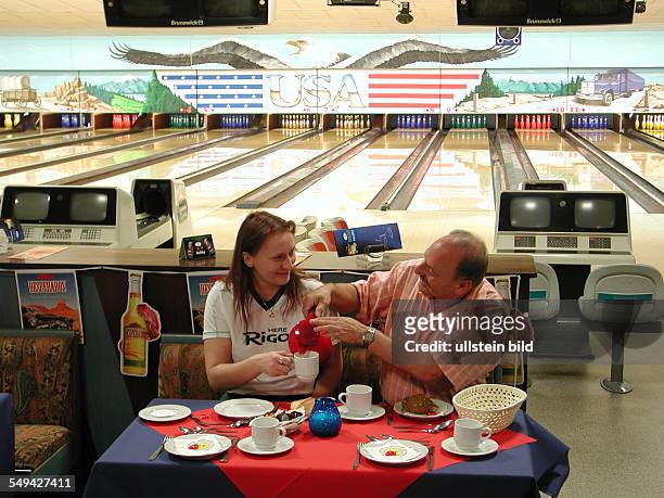 Germany: Bowling alley.- A couple eating breakfast at a laided table.