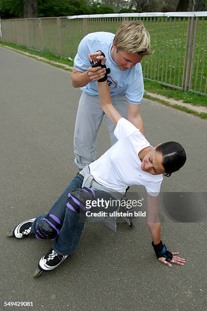 Germany, : Free time.- A girl falled with her inline skates; a boy is helping her to stand up.