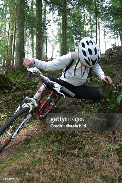 Germany, : A young woman falling off her mountainbike while she was riding through the wood.