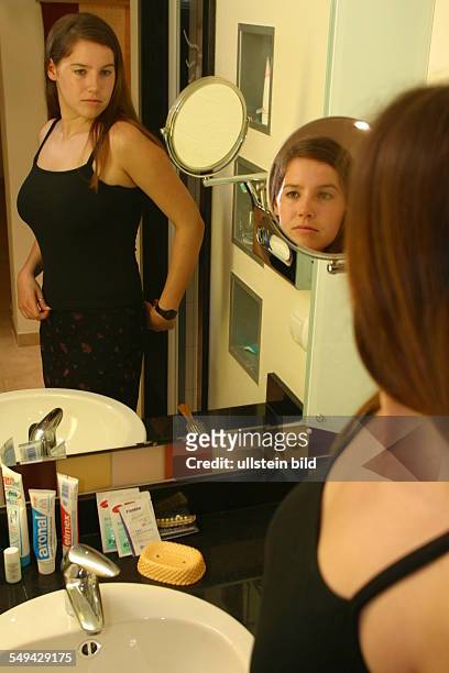 Germany, : A young woman lokking at herself in the mirror.