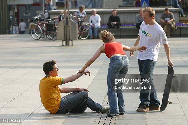 Germany, Cologne: Youth in their free time.- Young men skateboarding on the square in front of the cathedral; argument after a fall. A young woman...