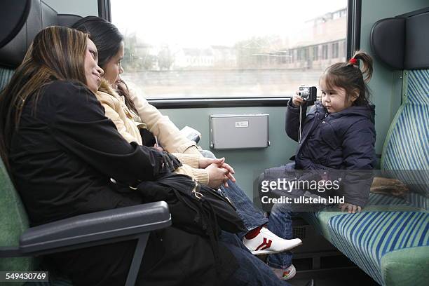 Germany, Dortmund: In a train.- A 4 years old girl is taking pictures of her mother and friends with a digital camera.