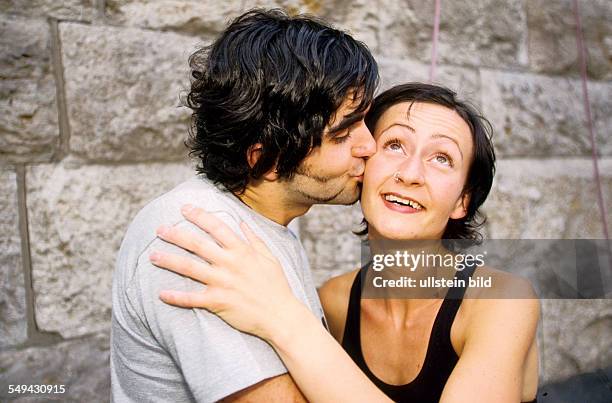 Germany: Free time.- Young persons after climbing; a man is kissing a woman on her cheek.