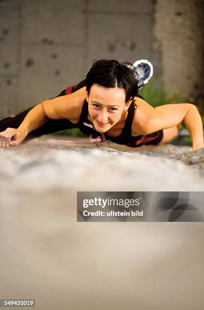 Germany: Free time.- A young woman climbing up a stone wall.