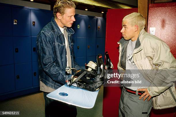 Germany: Free time.- Two young men talking next to the lockers; one of them is holding a snowboard in his hands.