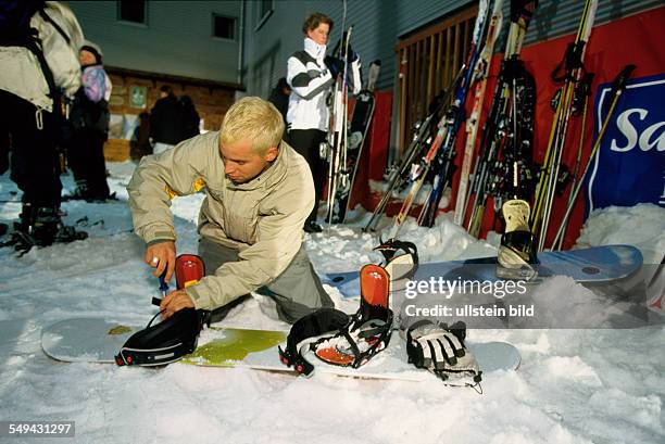 Germany: Free time.- A young man in the snow; he is screwing at his snowboard.