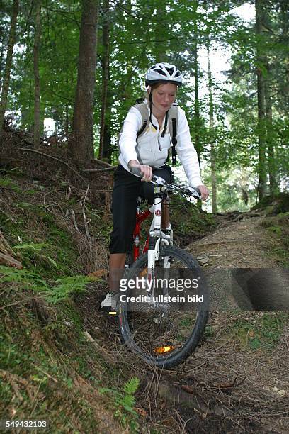 Germany, : A young woman riding with her mountainbike through the wood.