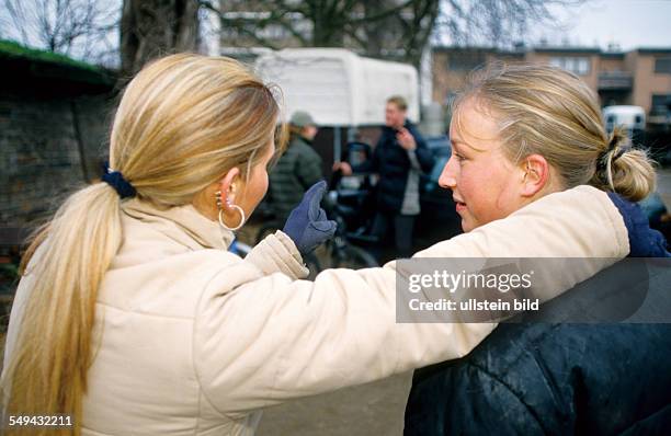 Germany: Free time.- Two young women on a stud farm; they are talking and watching two others.