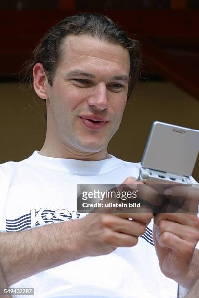 Germany, : Portrait of a young man; he is playing with a gameboy.