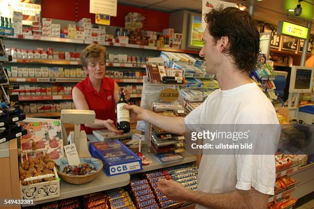 Germany, Kalkar, : Filling station.- At the counter; the cashier is handing a customer a bottle of wine.