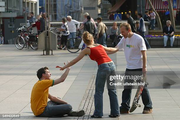 Germany, Cologne: Youth in their free time.- Young men skateboarding on the square in front of the cathedral; argument after a fall. A young woman...