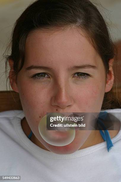 Germany, : Portrait of a young woman; she is making a chewing gum bubble.