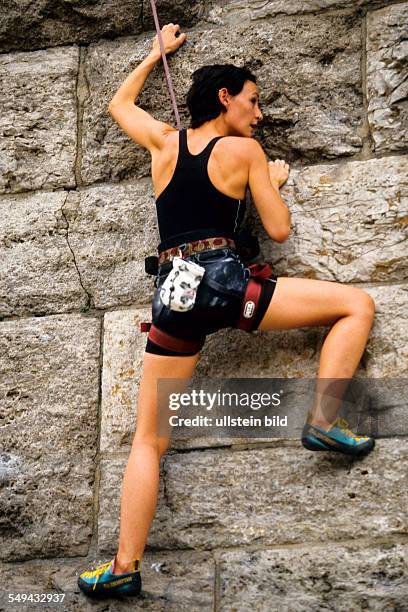 Germany: Free time.- A young woman climbing up a stone wall.