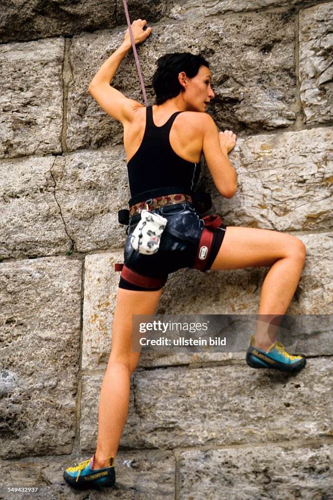 DEU, Germany: Free time.- A young woman climbing up a stone wall.