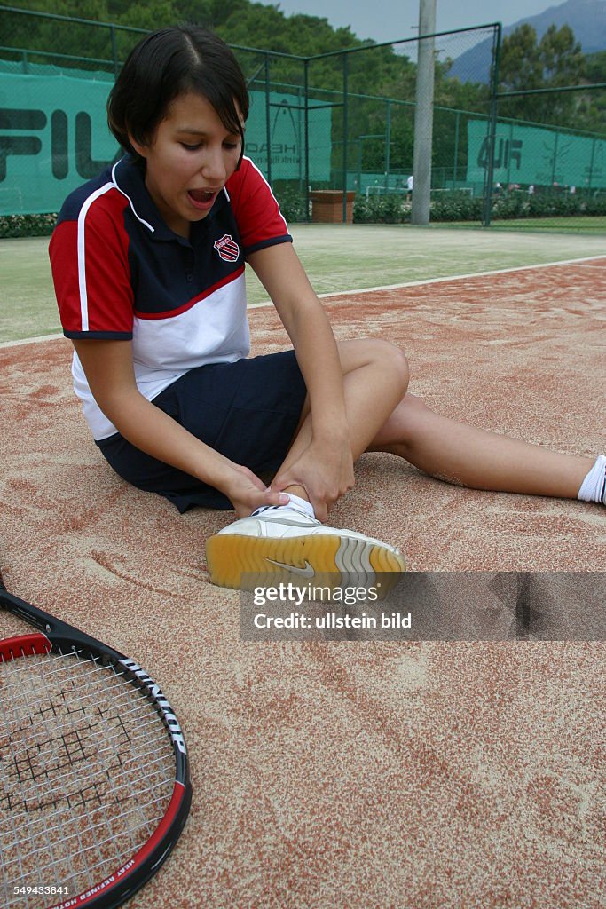 DEU, Germany, 24.11.2003: On the tennis court.- A young woman is holding her foot because she twisted her ankle.