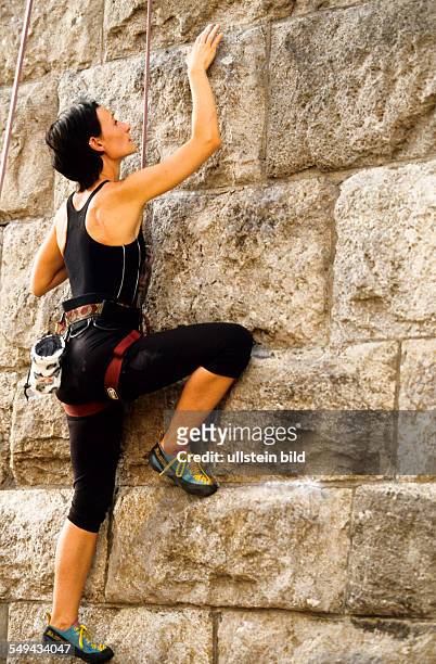 Germany: Free time.- A young woman climbing up a stone wall.
