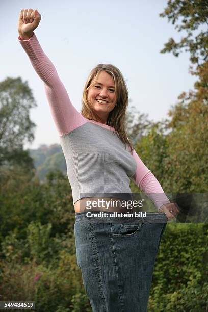 Germany, Essen: Portrait of a young mother.- She showing one of her old jeans after her diet.