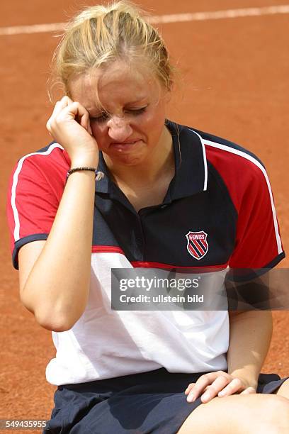 Germany, : Portrait of a young woman on a tennis court.- She is sitting on the court crying.