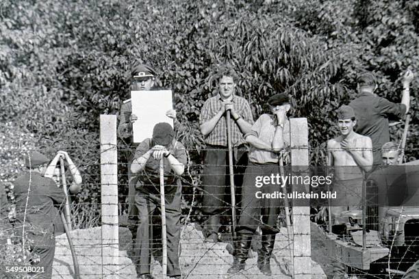 East Berlin policeman is trying to blind someone on the West Berlin side who is taking a picture of reinforcement works on the sector border at the...