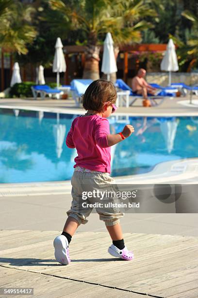 Ein Kleinkind, kleines Mädchen mit Sonnenbrille läuft am Beckenrand eines Schwimmbassin in einem Ferienclub Manavgat, Türkey,