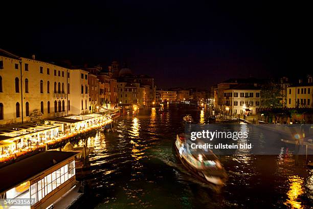 Brücke Ponte Scalzi über den Canale Grande . Restaurants sind erleuchtet, ein Boot fährt durch die Brücke. Lichter spiegeln sich im Wasser.